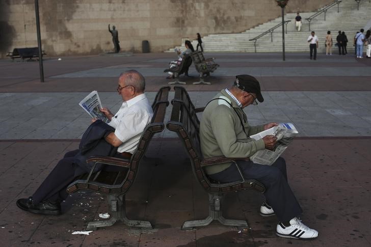 © Reuters. Pensioners read a free newspaper as they sit on public benches in Madrid