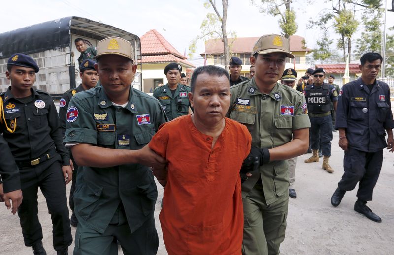 © Reuters. Yem Chrin is escorted by police officers upon arrival at the Provincial Court of Battambang