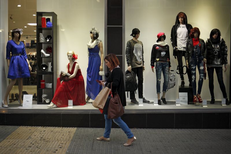 © Reuters. A woman checks her mobile phone as she walks past a showcase of a clothing store during the Black Friday sales in Malaga