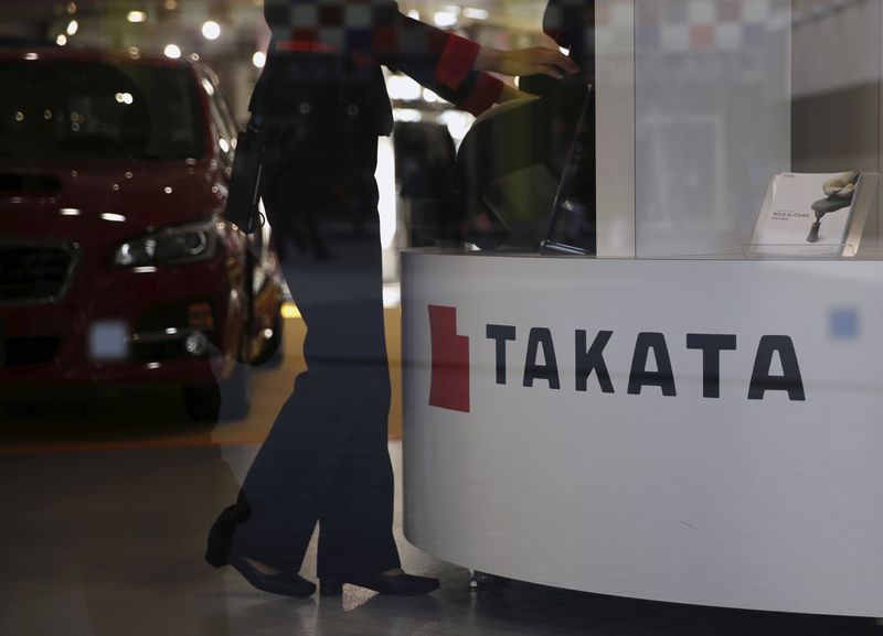 © Reuters. A woman stands next to a logo of Takata Corp at a showroom for vehicles in Tokyo