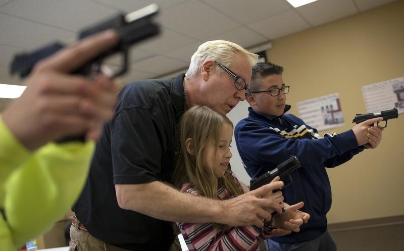 © Reuters. Instructor Jerry Kau shows student Joanna Zuber how to hold a handgun alongside Sam Minnifield during a Youth Handgun Safety Class at GAT Guns in East Dundee
