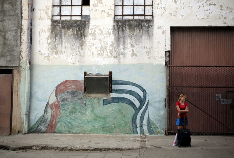 © Reuters. A student stands near graffiti of the colours of Fidel Castro's 26th of July Movement and the Cuban flag in Vertientes