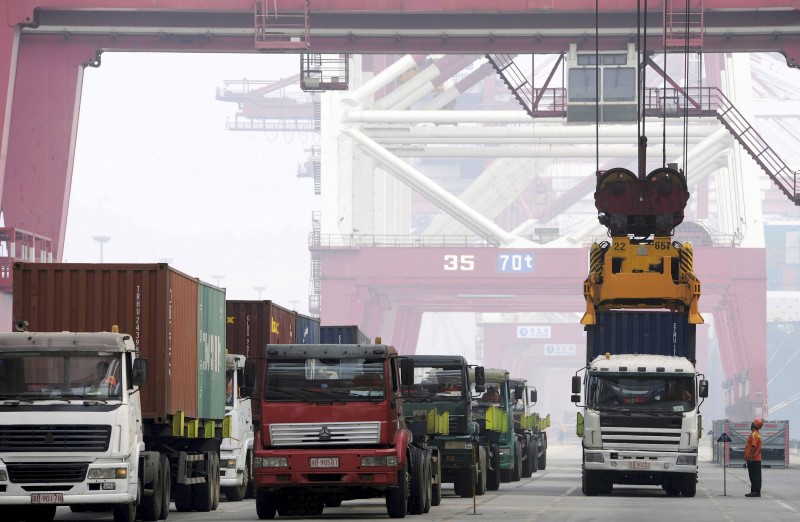 © Reuters. Crane lifts a shipping container from a truck to load it onto a ship at a port in Qingdao, Shandong province, China