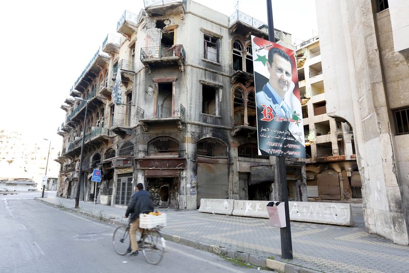 © Reuters. A man rides a bicycle past a poster depicting Syria's President Bashar al-Assad near the new clock square in the old city of Homs