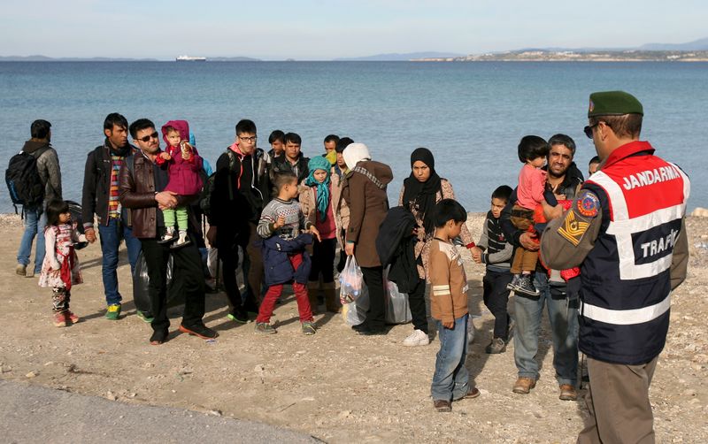 © Reuters. A Turkish Gendarme leads a group of refugees to buses to prevent them from sailing off for the Greek island of Chios by dinghies, at a beach in the western Turkish coastal town of Cesme