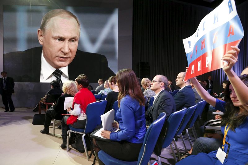 © Reuters. A journalist holds up a poster to get attention and ask a question during Russian President Vladimir Putin's annual end-of-year news conference in Moscow