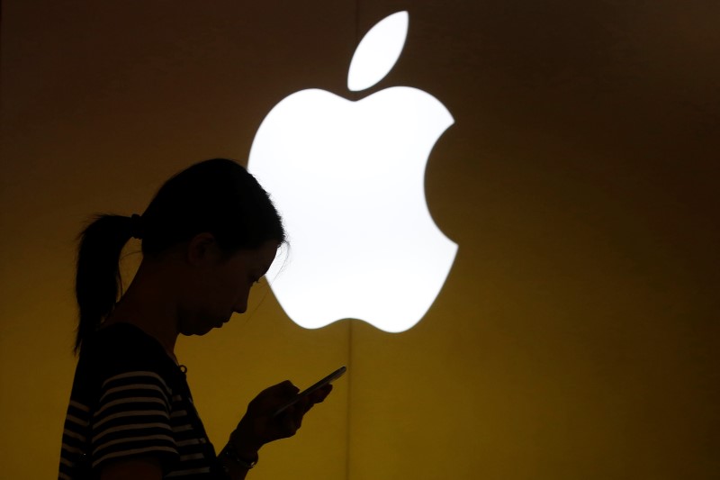 © Reuters. A woman looks at the screen of her mobile phone in front of an Apple logo outside an Apple store in downtown Shanghai