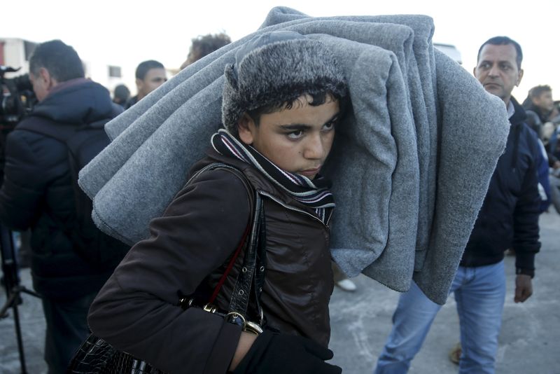 © Reuters. A migrant boy carries blankets as refugees and migrants arrive aboard the passenger ferry Eleftherios Venizelos from the island of Lesbos at the port of Piraeus