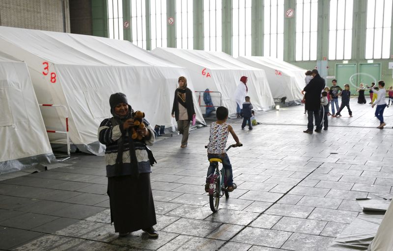 © Reuters. Migrants walk next to tents in a shelter for migrants inside a hangar of the former Tempelhof airport in Berlin