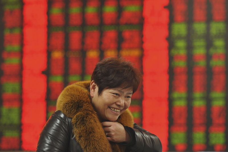 © Reuters. An investor smiles in front of an electronic board showing stock information at a brokerage house in Fuyang