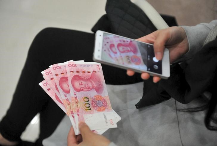 © Reuters. A woman takes pictures of new 100 yuan banknotes she withdrew from a bank in Hangzhou