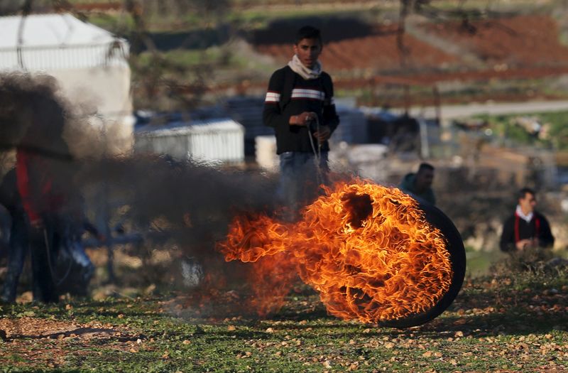 © Reuters. Palestinian protester stands behind a burning tyre during clashes with Israeli troops, near Israel's Ofer Prison near the West Bank city of Ramallah