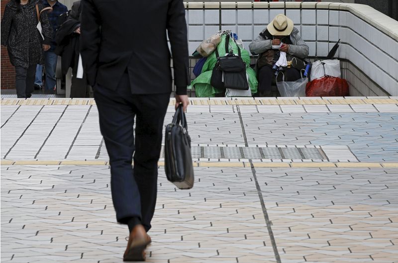 © Reuters. A man (R) sits in a street as a businessman walks nearby at a business district in Tokyo