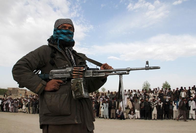 © Reuters. A member of the Taliban insurgent and other people stand at the site during the execution of three men in Ghazni Province