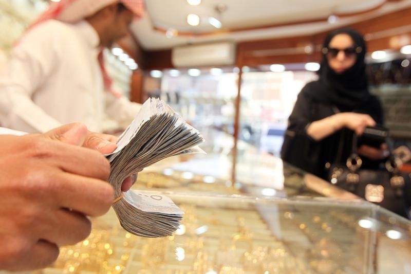 © Reuters. A salesman counts money as a woman walks past a jewellery shop at the gold market in Riyadh