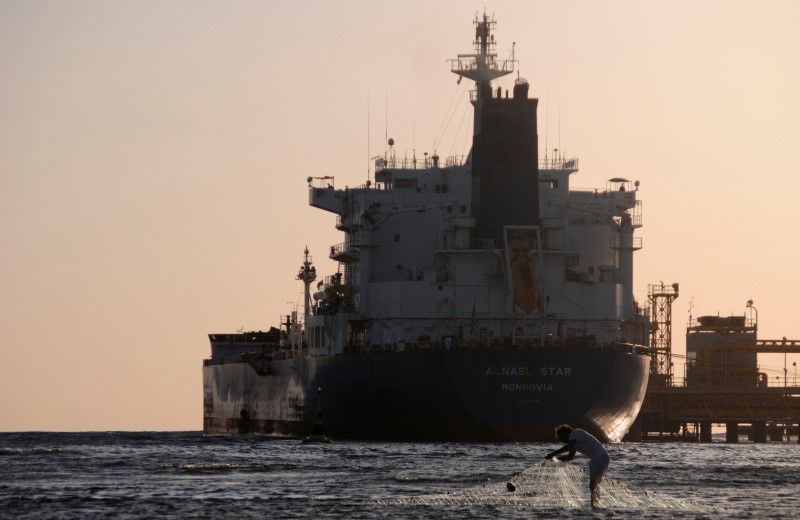 © Reuters. Fisherman pulls in his net as an oil tanker is seen at the port in the northwestern city of Duba