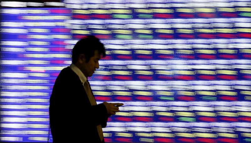 © Reuters. Man holding a mobile phone walks past an electronic stock quotation board outside a brokerage in Tokyo