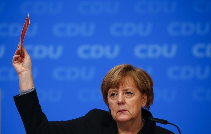 © Reuters. German Chancellor and leader of the CDU Merkel holds up her voting card during a vote on a resolution about refugees at the CDU party congress in Karlsruhe