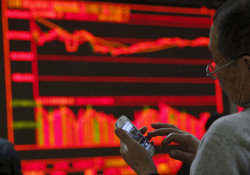 © Reuters. A man checks his mobile phone in front of an electronic board at a brokerage house in Beijing