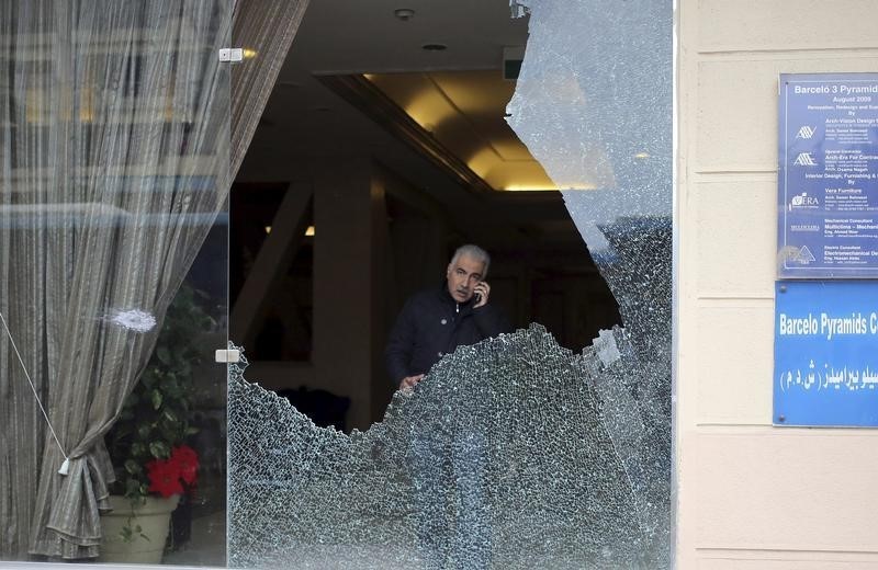 © Reuters. A police investigator is seen through a smashed window at a hotel where gunmen attacked tourists in front of a hotel in Giza