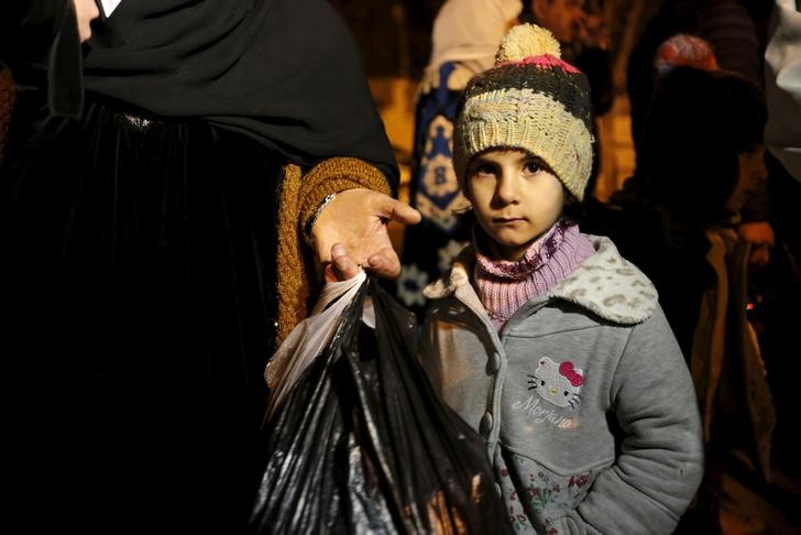 © Reuters. Menina síria espera com a família ao sair de Madaya após a chegada de um combio de ajuda humanitária à cidade