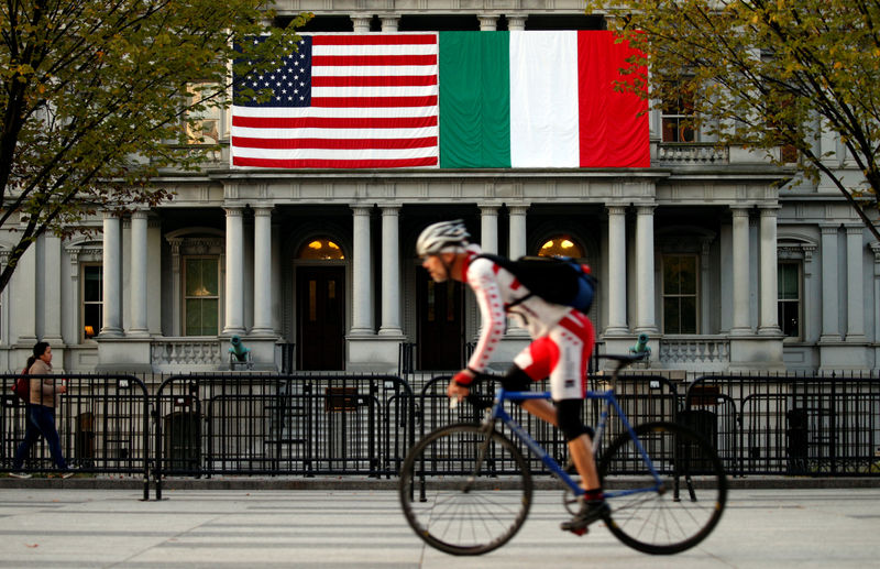 © Reuters. A cyclist passes flags of the U.S. and Italy draped over the Eisenhower Executive Office Building beside the White House in Washington