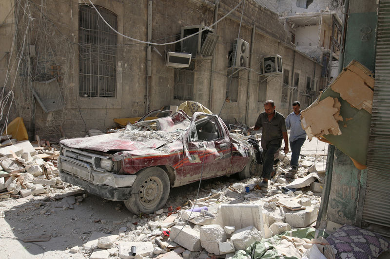 © Reuters. People walk near a damaged vehicle after an air strike Sunday in the rebel-held besieged al-Qaterji neighbourhood of Aleppo