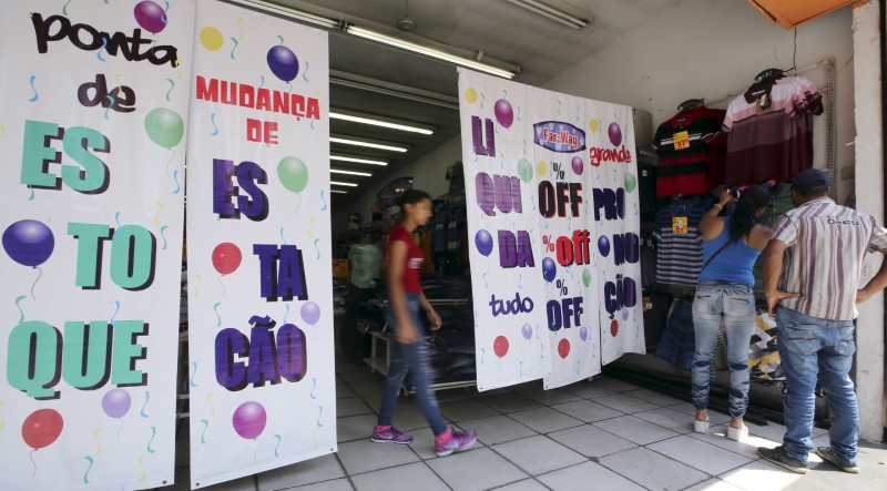 © Reuters. Customers shop near signs advertising promotional sales at a clothing store in Sao Paulo, Brazil