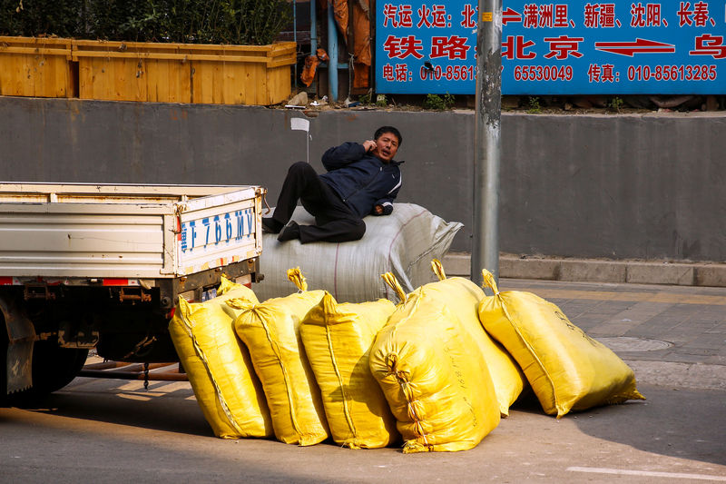 © Reuters. A worker sits on top of sacks with construction material, outside a construction site in Beijing