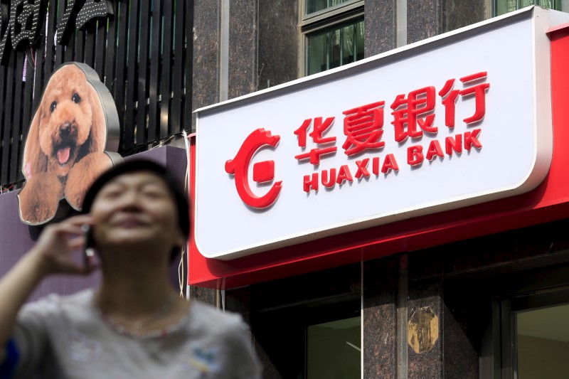 © Reuters. Woman speaks on her mobile phone as she walks past a Hua Xia Bank branch in Shanghai, China