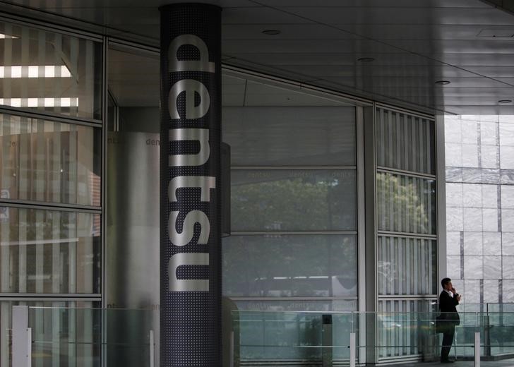 © Reuters. A man speaks on his mobile phone near a logo of Dentsu Co. at the entrance of the company headquarters in Tokyo
