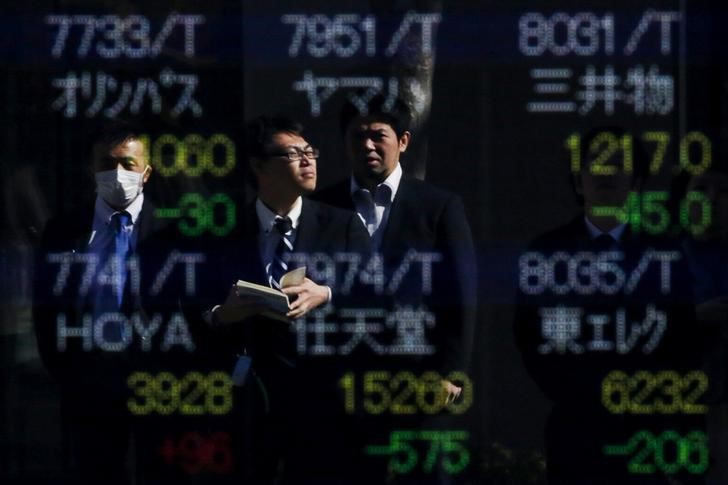© Reuters. Tokyo, passanti davanti a un tabellone di un brokerage con gli indici di borsa