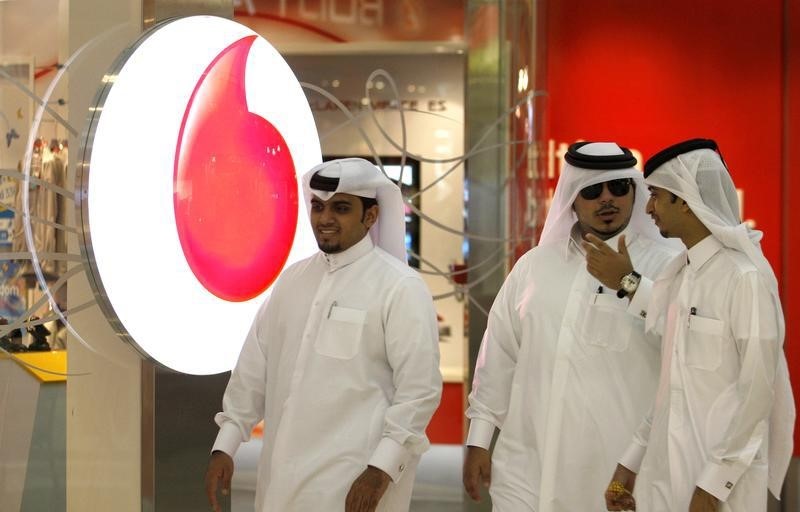 © Reuters. Men walk past a Vodafone-Qatar Telecommunication in Doha