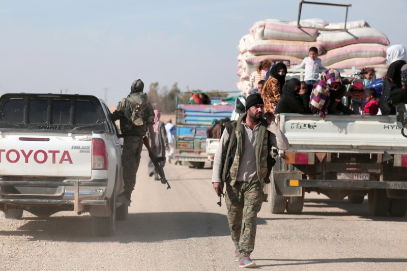 © Reuters. A Syrian Democratic Forces (SDF) fighter walks near vehicles carrying people fleeing clashes in Tweila'a village and Haydarat area, north of Raqqa city