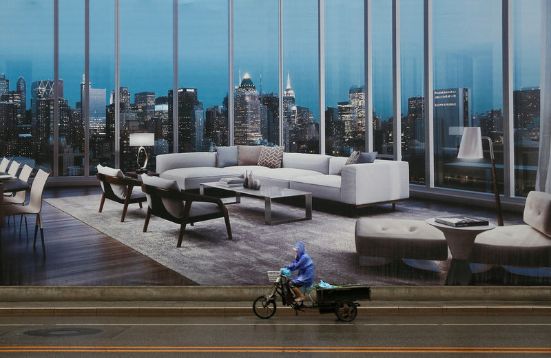 © Reuters. A man rides a tricycle past an advertising poster for luxury apartments in Beijing,