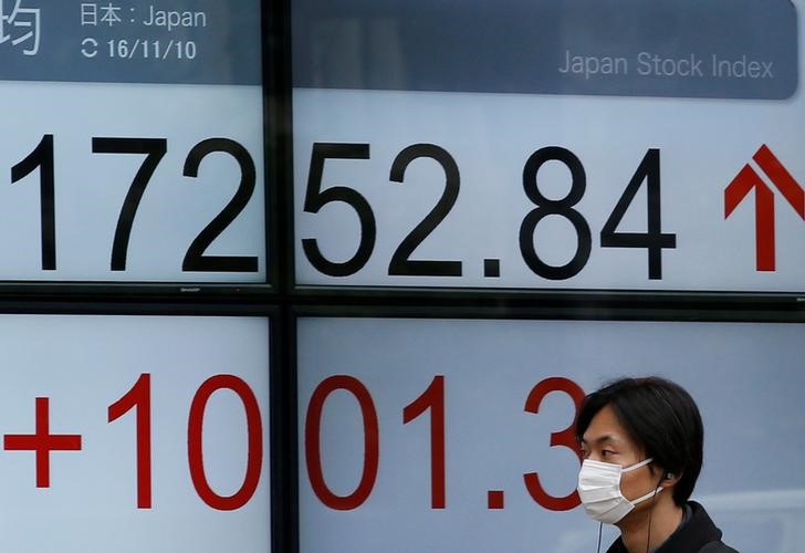 © Reuters. A man walks in front of an electronic board showing Japan's Nikkei average outside a brokerage in Tokyo