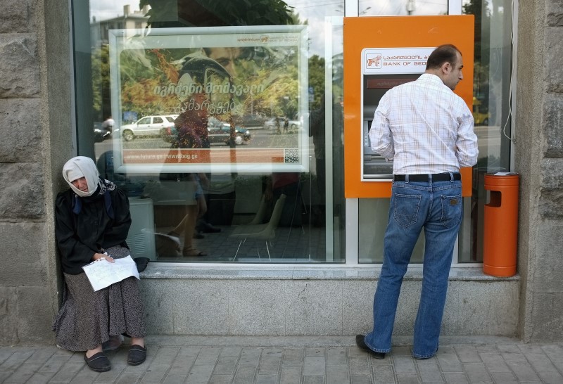 © Reuters. A man uses an automated teller machine next to a woman begging for money on the street in the Georgian capital Tbilisi