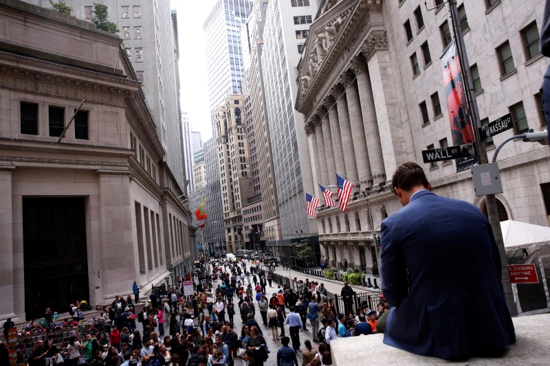 © Reuters. A man sits on a marble wall as pedestrians walk on the streets in front of the New York Stock Exchange in New York