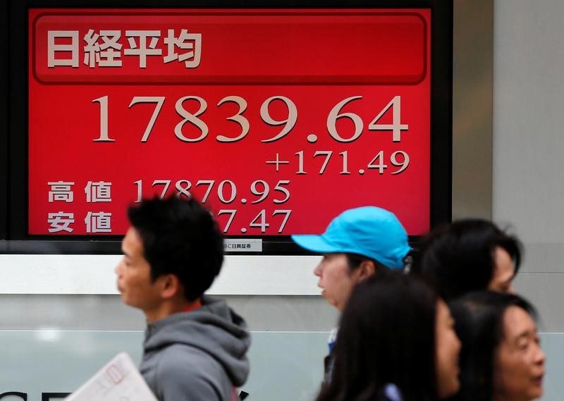 © Reuters. People walk past an electronic board showing Japan's Nikkei average outside a brokerage in Tokyo