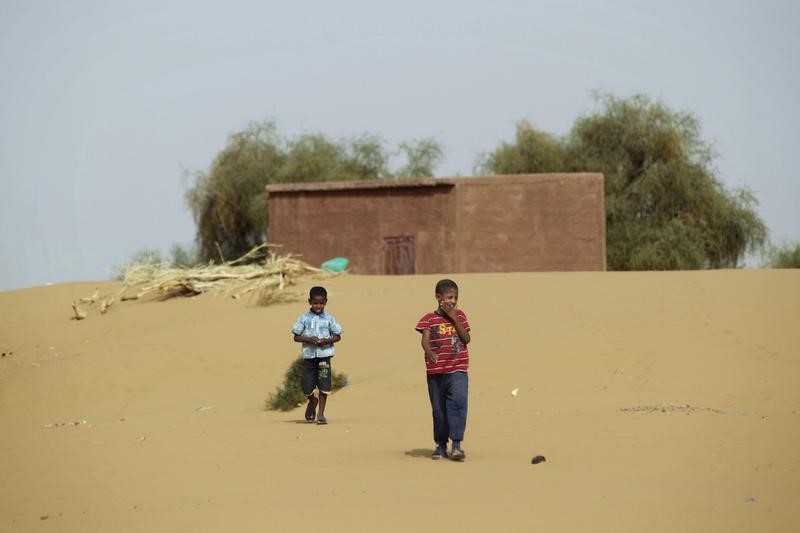 © Reuters. Boys walk on desert sands in the town of Moghtar-Lajjar