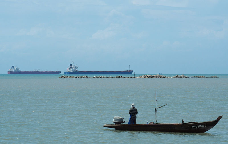 © Reuters. A dry bulk ship passes a fisherman off the coast of Johor