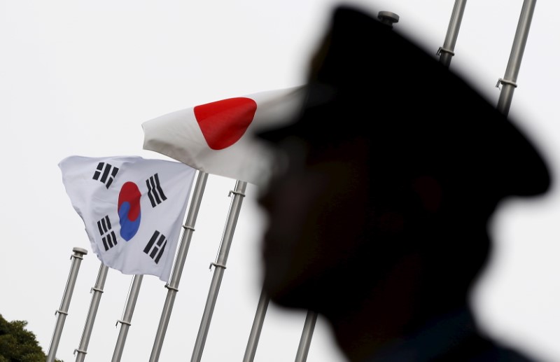 © Reuters. Police officer stands guard near Japan and South Korea national flags at hotel, where South Korean embassy in Japan is holding the reception to mark the 50th anniversary of normalisation of ties between Seoul and Tokyo in Tokyo