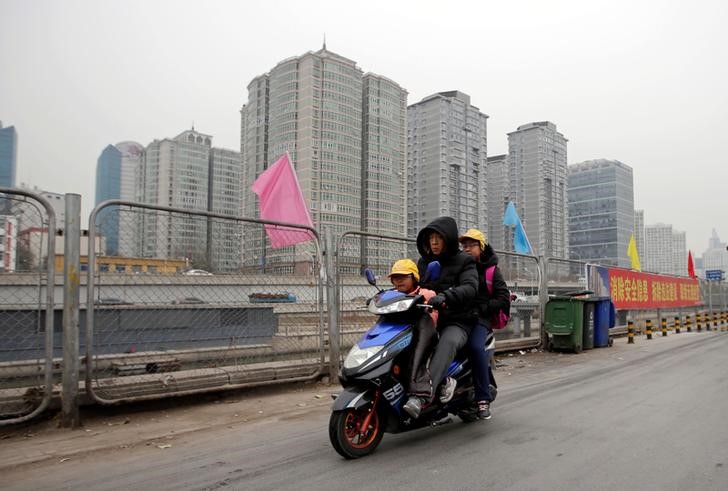 © Reuters. A man rides an electric bike, carrying children near apartment blocks in Beijing