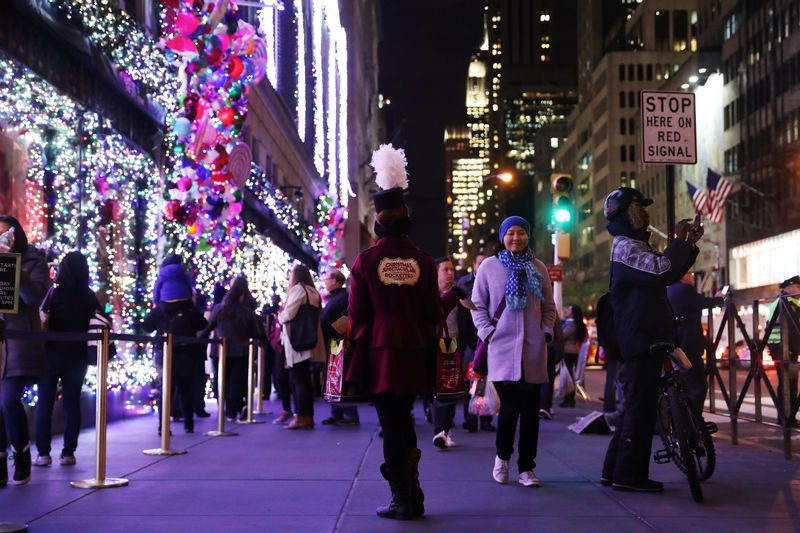 © Reuters. A woman hands out fliers for the Radio City Christmas Spectacular as people pass holiday window displays at Saks Fifth Avenue in New York