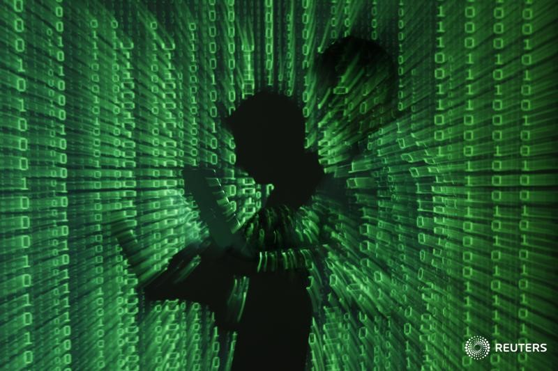 © Reuters. Бинарный код проецируется на мужчину с ноутбуком в офисе в Варшаве