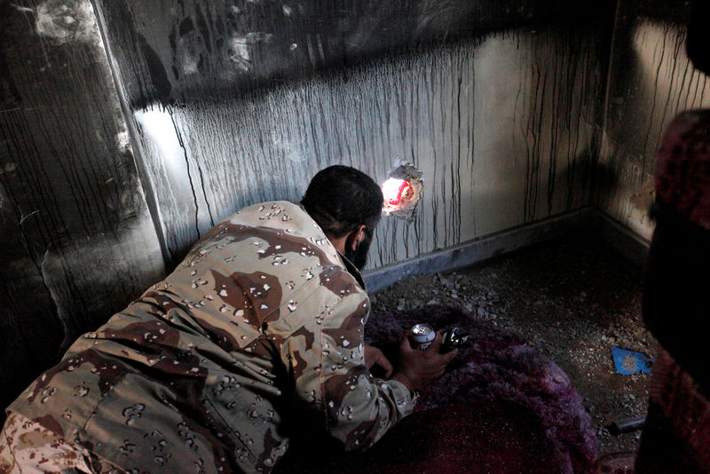 © Reuters. Fighter of Libyan forces allied with the U.N.-backed government looks for Islamic State militants through a hole in a wall as forces advance against the militants' holdouts in Ghiza Bahriya district in Sirte