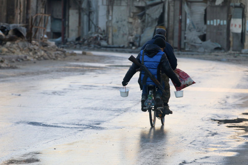 © Reuters. A rebel fighter carries food while riding a bicycle and carrying his weapon on his back in rebel-held besieged old Aleppo