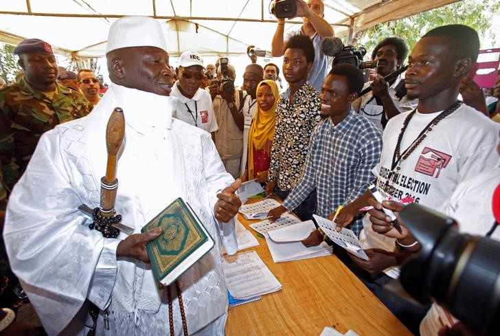 © Reuters. Gambian President Jammeh holds a copy of the Quran while speaking to a poll worker at a polling station during the presidential election in Banjul