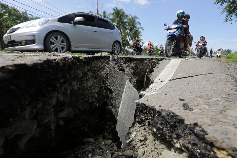 © Reuters. Motorcyclists pass a damaged section of a road following an earthquake in Meuredu, Pidie Jaya, in the northern province of Aceh