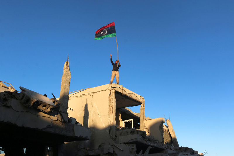 © Reuters. Fighter of Libyan forces waving a Libyan flag flashes victory sign as he stands atop the ruins of a house after forces finished clearing Ghiza Bahriya, the final district of the former Islamic State stronghold of Sirte